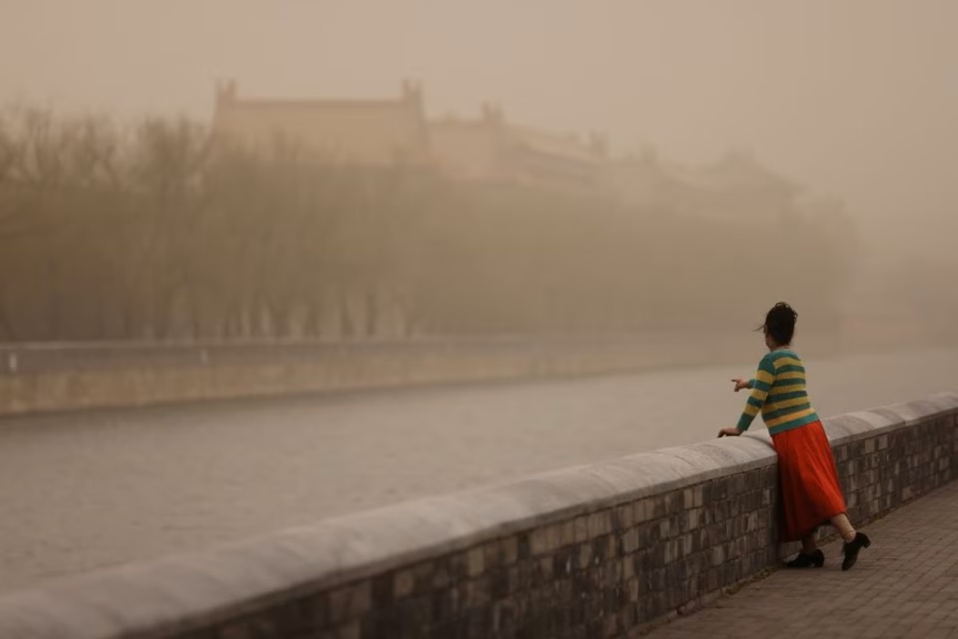 Một người phụ nữ tạo dáng chụp ảnh gần Tử Cấm Thành, kh Bắc Kinh bị sương mù bao phủ giữa một cơn bão cát